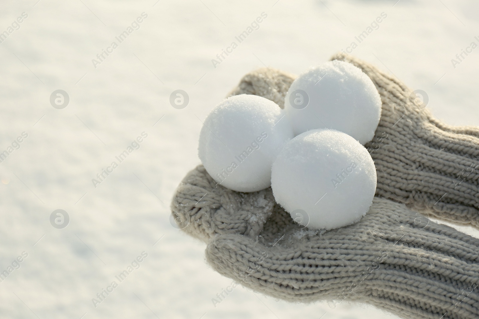 Photo of Woman in knitted mittens holding snowballs outdoors, closeup. Space for text