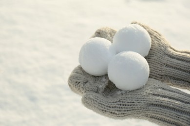 Photo of Woman in knitted mittens holding snowballs outdoors, closeup. Space for text
