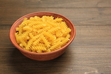 Raw fusilli pasta in bowl on wooden table, closeup. Space for text
