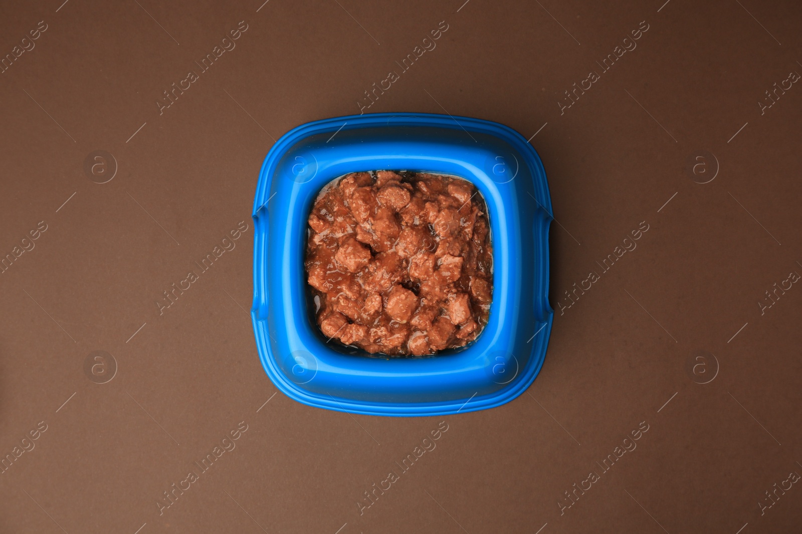 Photo of Wet pet food in feeding bowl on brown background, top view