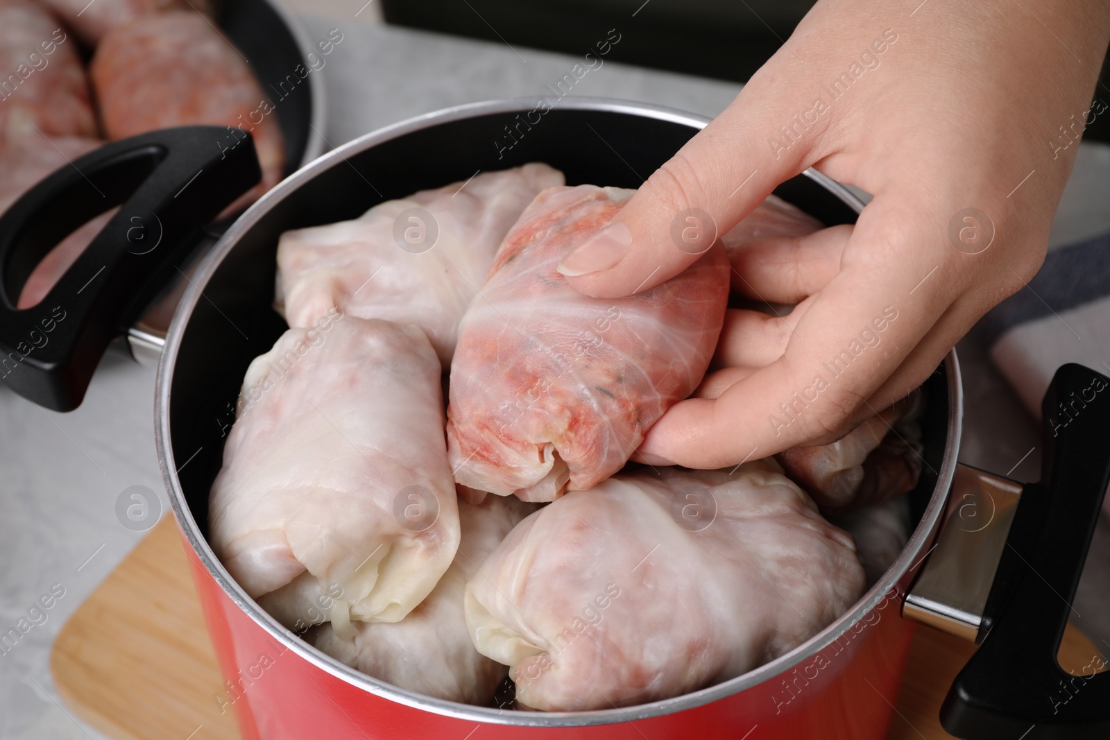 Photo of Woman putting uncooked stuffed cabbage roll into pot at light grey table, closeup