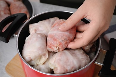 Photo of Woman putting uncooked stuffed cabbage roll into pot at light grey table, closeup