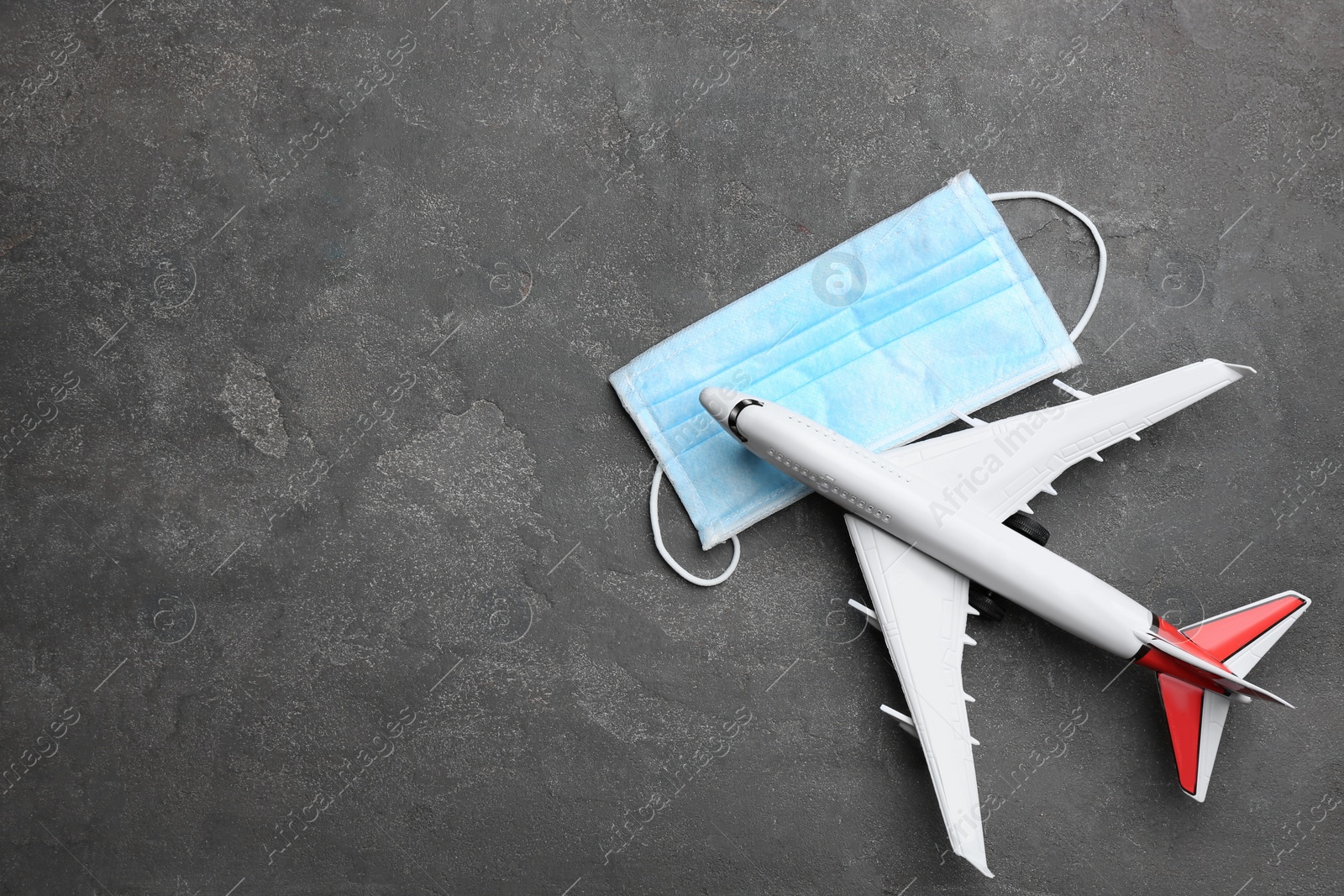 Photo of Toy airplane and protective mask on grey background, flat lay with space for text. Travelling during coronavirus pandemic