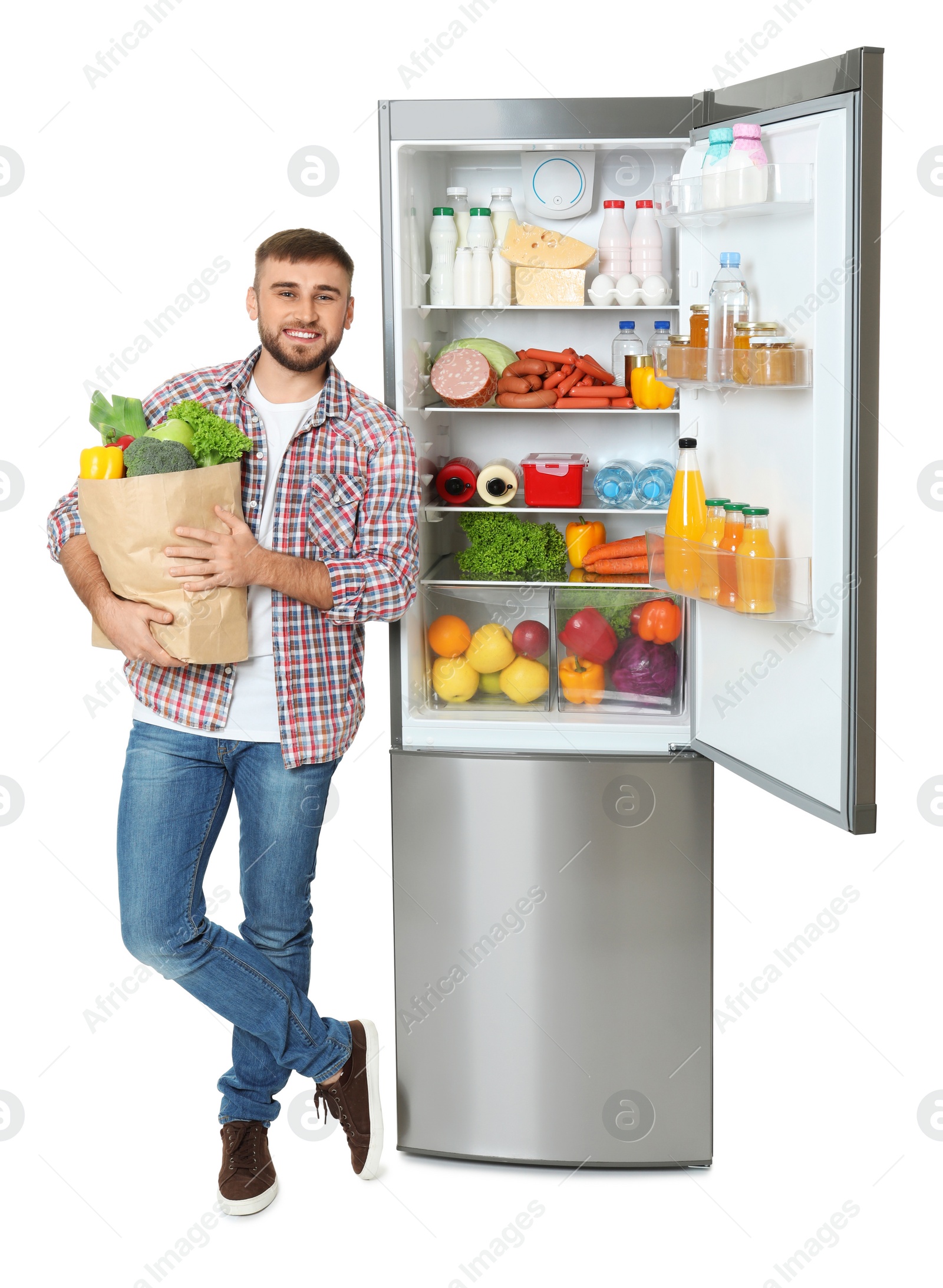 Photo of Young man with bag of groceries near open refrigerator on white background