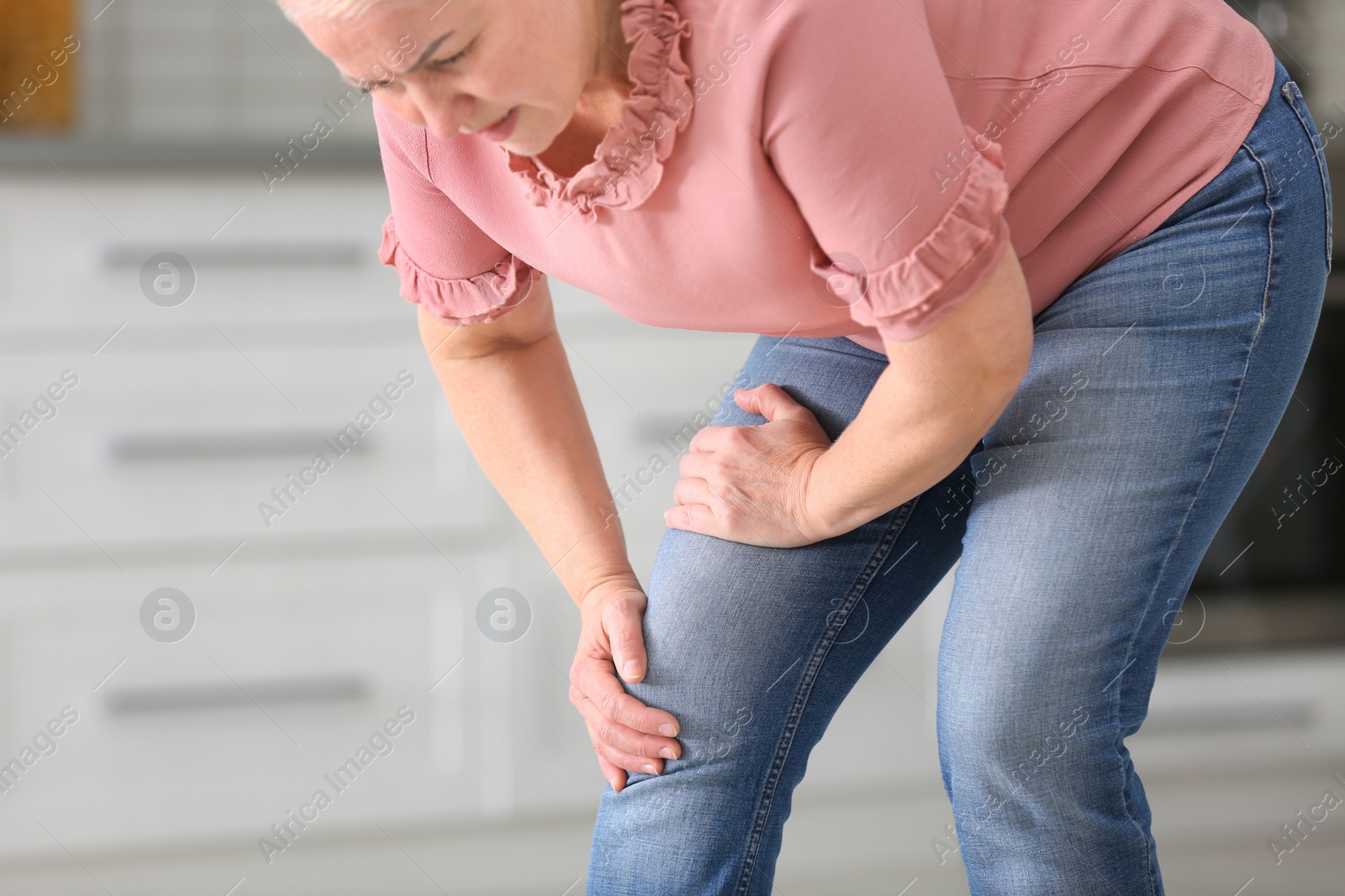 Photo of Senior woman suffering from knee pain in kitchen. Space for text