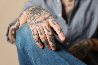 Photo of Young man with tattoos on arms against beige background, closeup