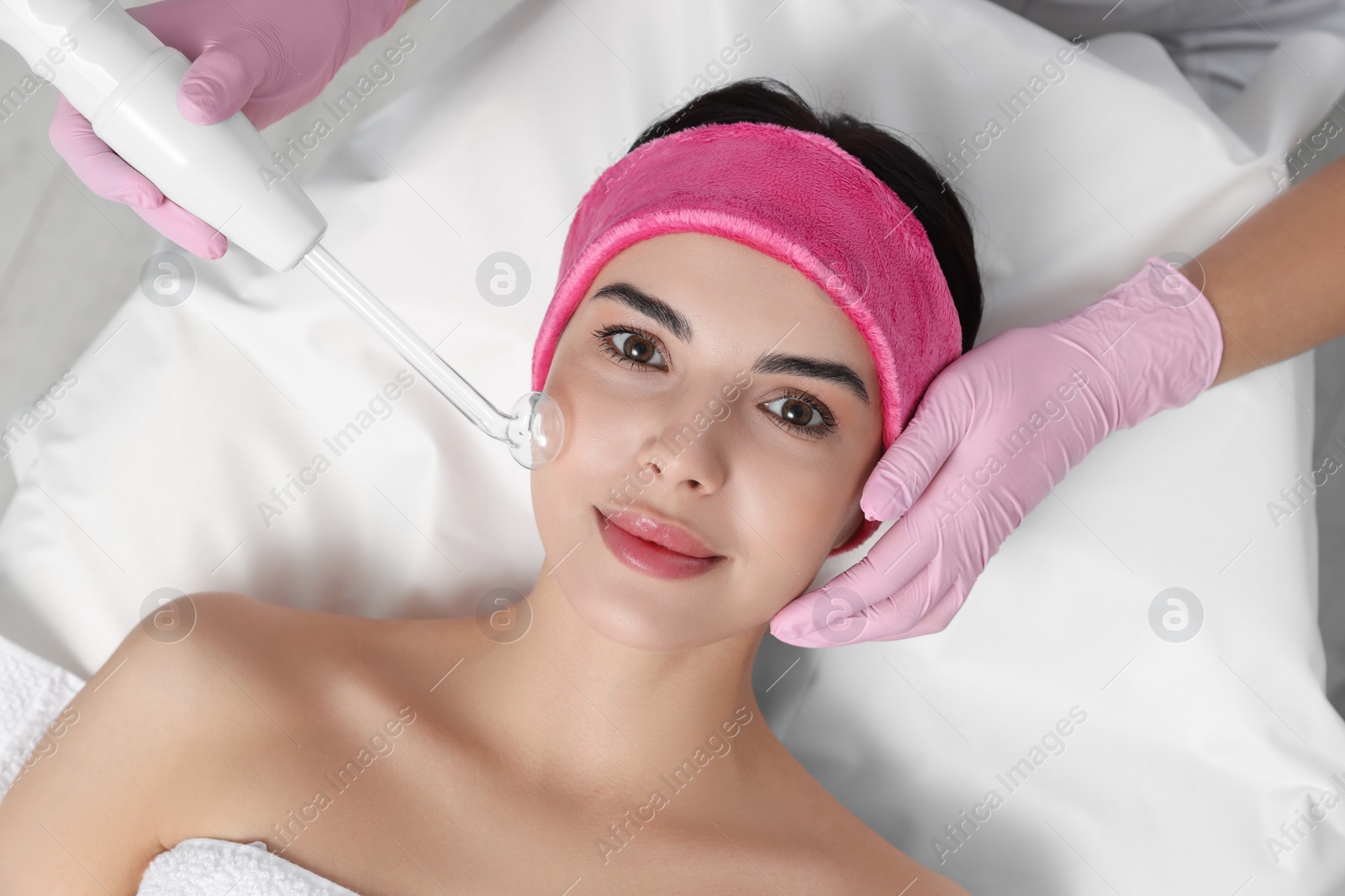 Photo of Young woman undergoing face rejuvenation procedure with darsonval in salon, top view