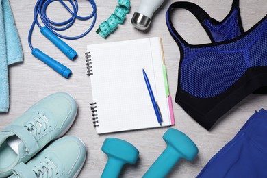 Photo of Notebook, clothes and sports equipment on white wooden table, flat lay. Personal training