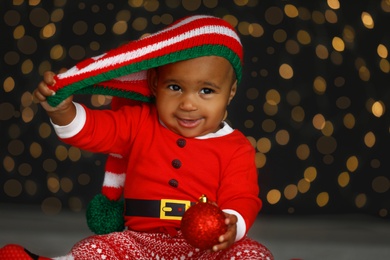 Image of Cute little African American baby with Christmas ball and blurred lights on dark background
