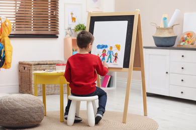 Photo of Little child painting on easel in room