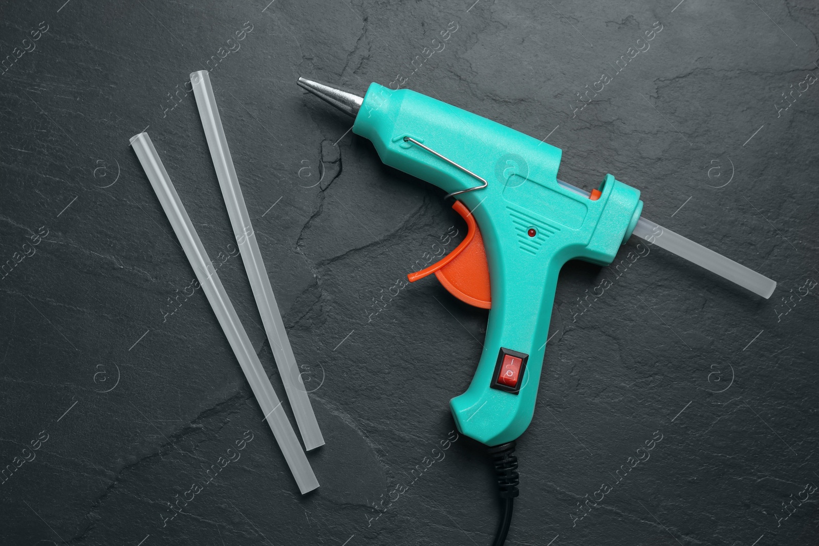 Photo of Turquoise glue gun and sticks on black table, flat lay