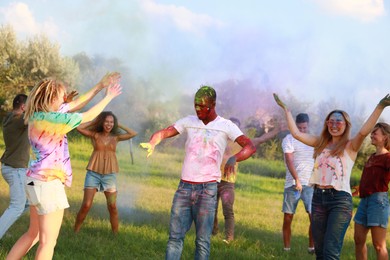 Happy friends having fun with colorful powder dyes outdoors. Holi festival celebration