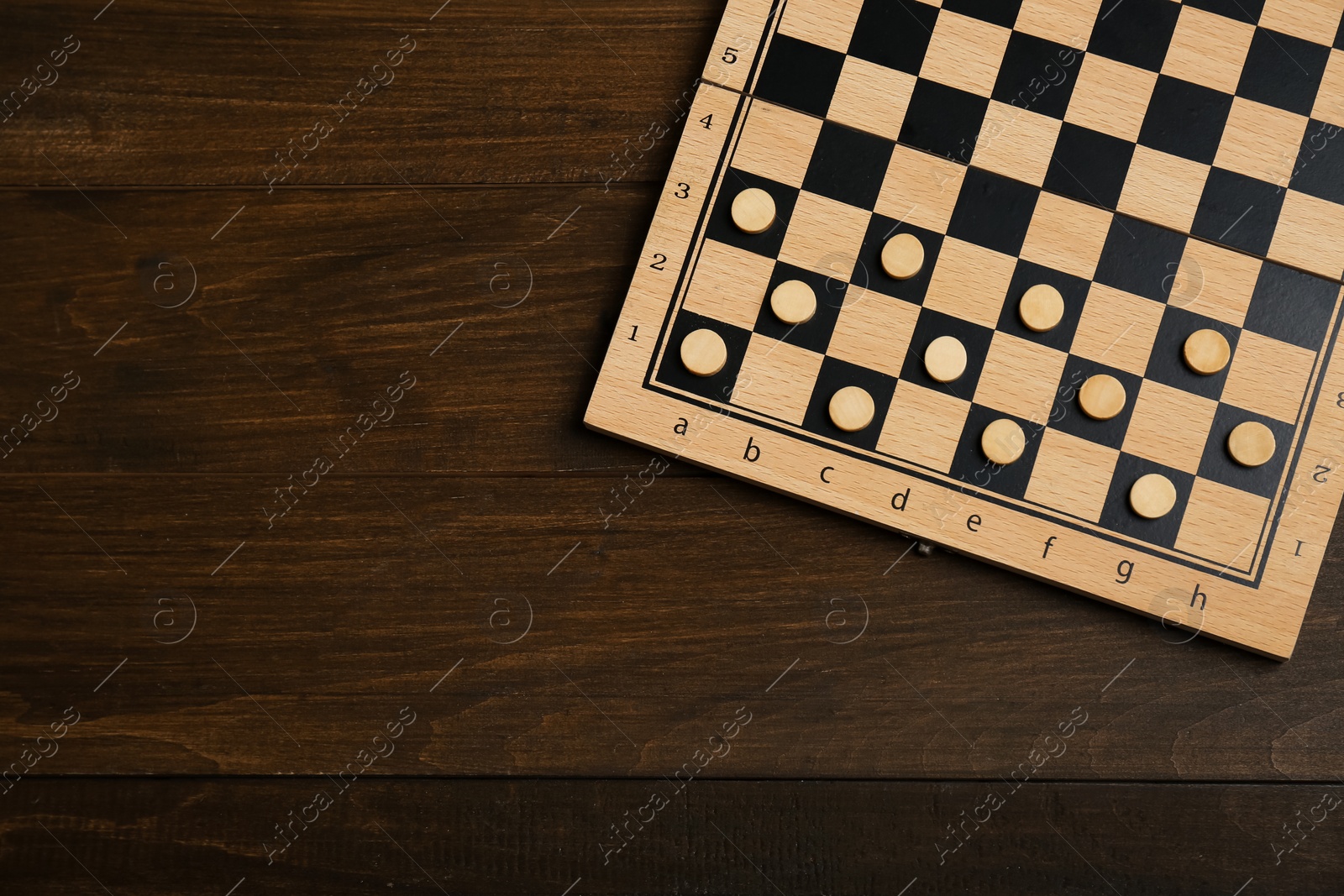 Photo of Checkerboard with game pieces on wooden table, top view. Space for text