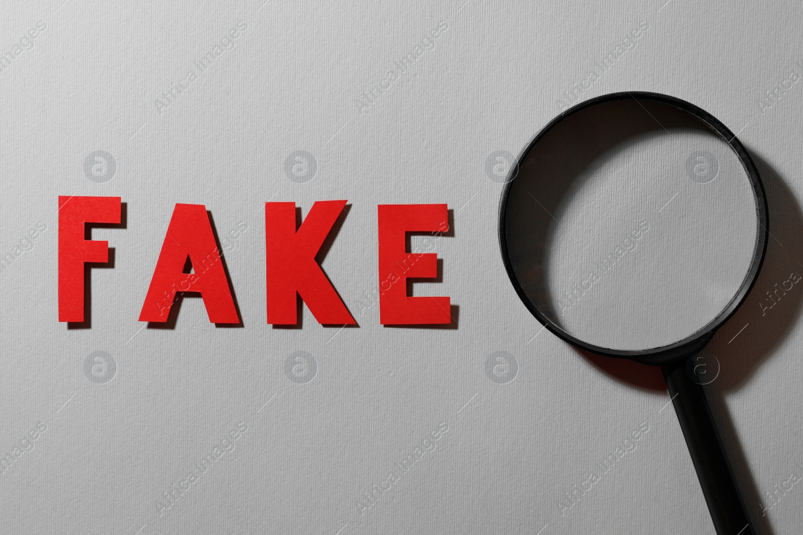 Photo of Word Fake made of red letters and magnifying glass on grey background, flat lay