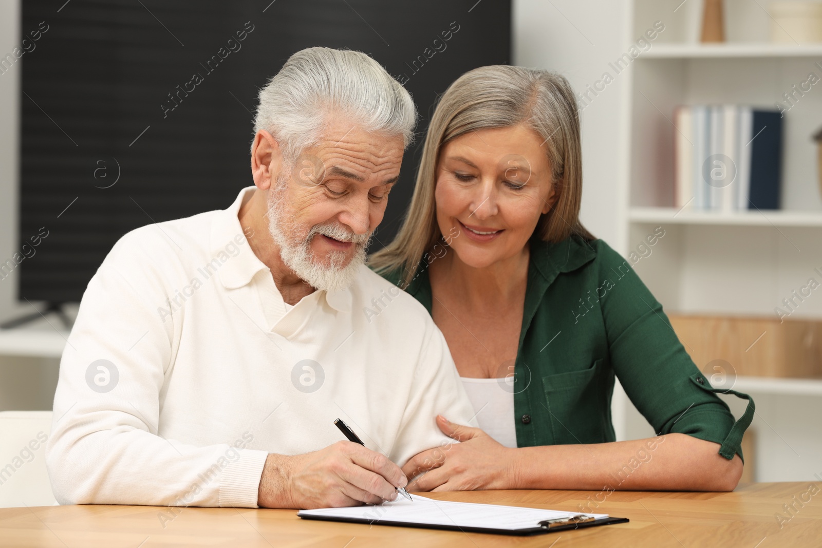 Photo of Senior couple signing Last Will and Testament indoors