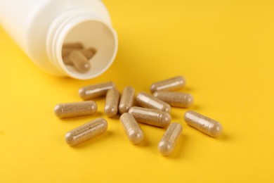 Photo of Vitamin capsules and medical bottle on yellow background, closeup