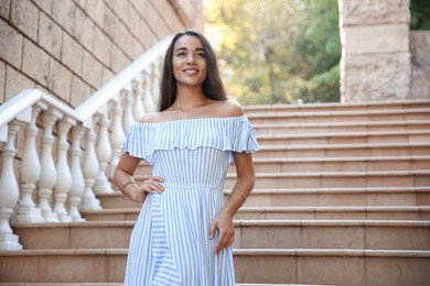 Photo of Beautiful young woman in stylish light blue striped dress on stairs outdoors
