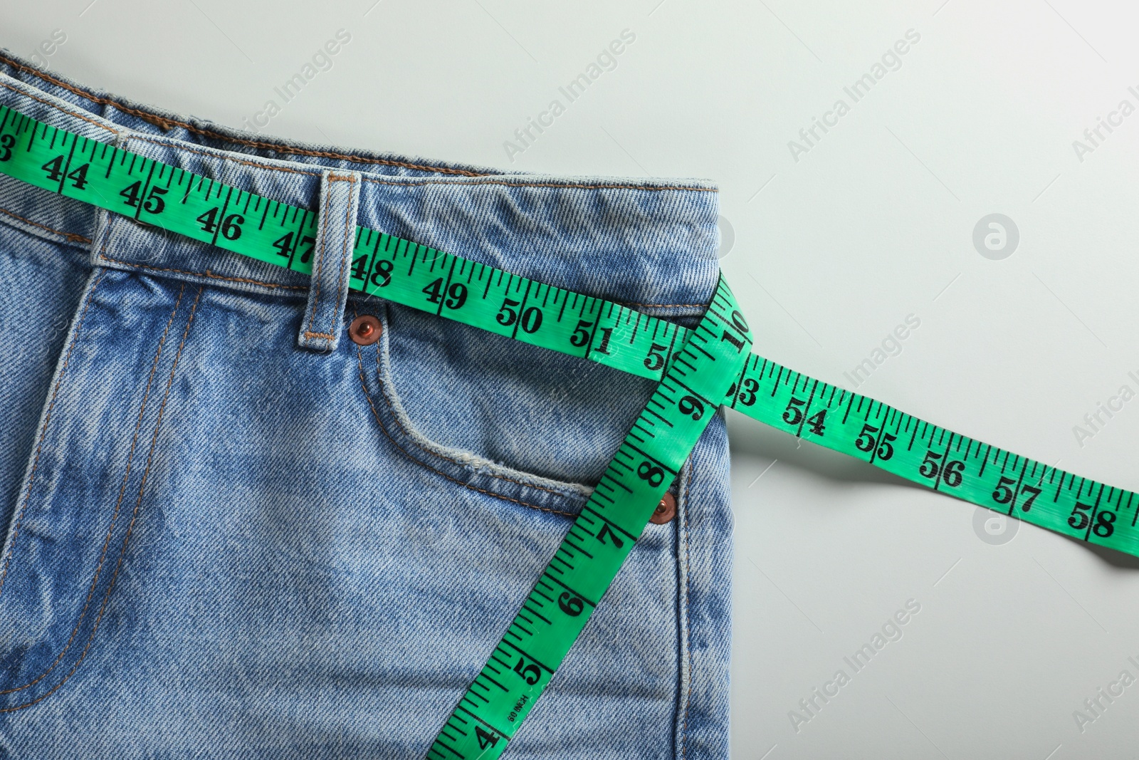 Photo of Jeans with measuring tape on light grey background, top view. Weight loss concept