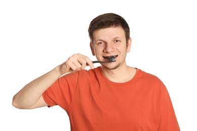 Man brushing teeth with charcoal toothpaste on white background