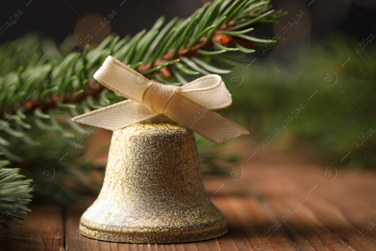 Photo of Bell with bow and fir branches on wooden table, closeup. Christmas decor