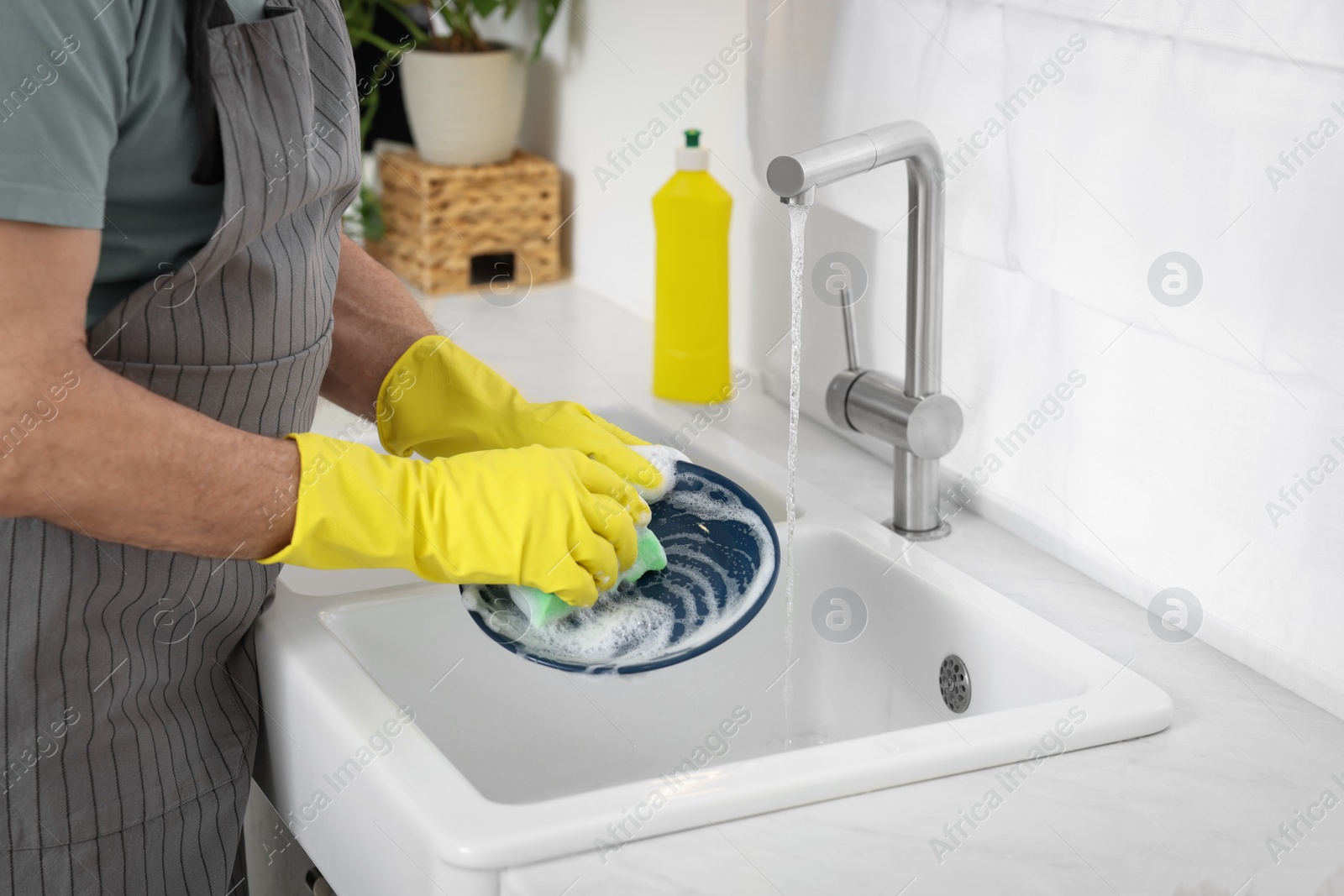 Photo of Man in protective gloves washing plate above sink in kitchen, closeup