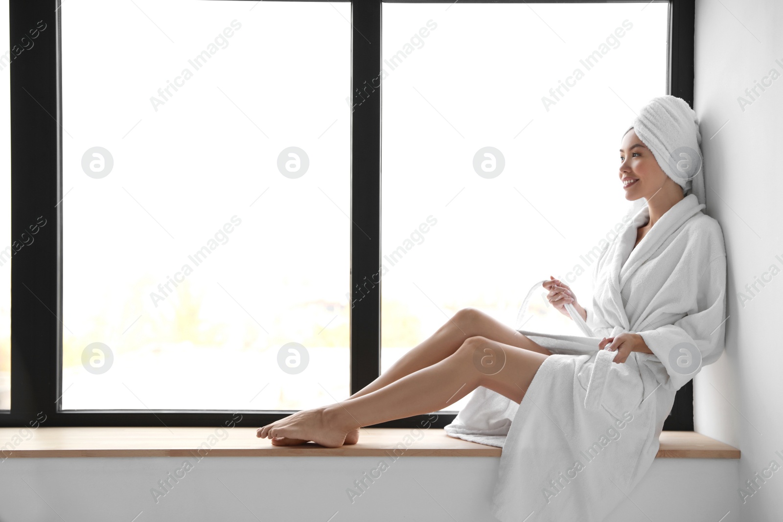 Photo of Young woman with towel wearing bathrobe near window