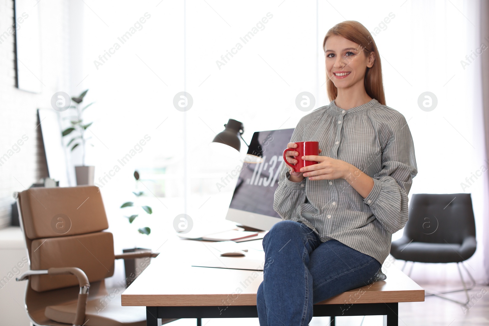 Photo of Young woman with cup of drink relaxing in office during break