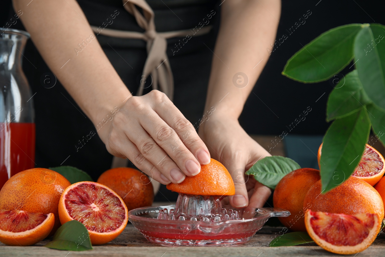 Photo of Woman squeezing sicilian orange juice at wooden table, closeup