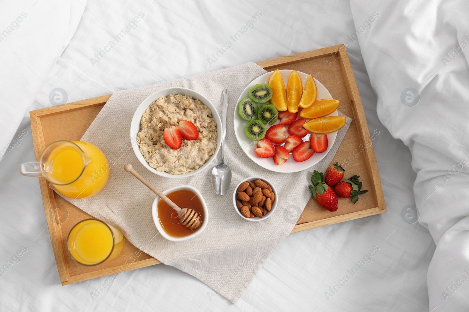 Tasty breakfast served in bed. Oatmeal, juice, fruits, almonds and honey on tray, top view Photo of Tasty breakfast served in bed. Oatmeal, juice, fruits, almonds and honey on tray, top view