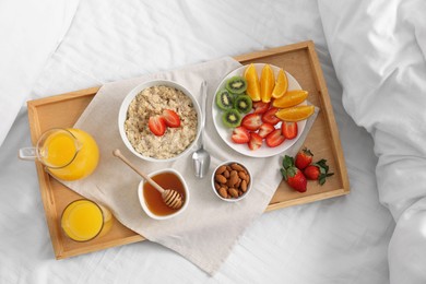 Photo of Tasty breakfast served in bed. Oatmeal, juice, fruits, almonds and honey on tray, top view