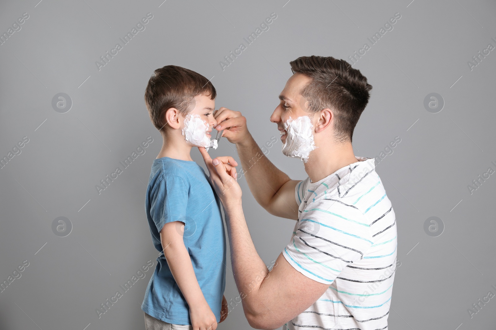 Photo of Dad pretending to shave his little son on color background