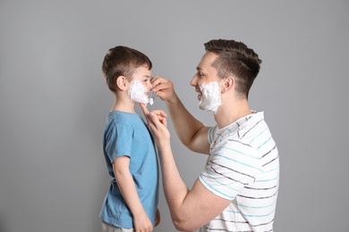 Photo of Dad pretending to shave his little son on color background