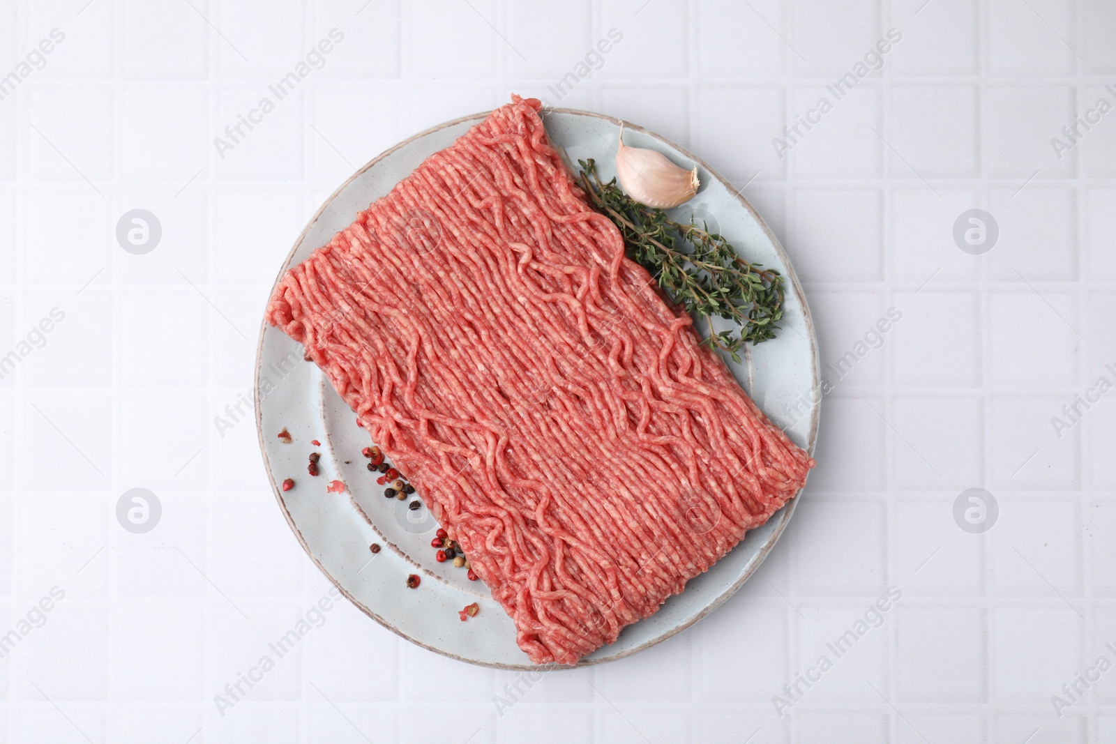 Photo of Fresh raw ground meat, peppercorns, garlic and thyme on white tiled table, top view