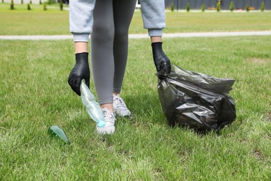 Photo of Woman with trash bag picking up glass and plastic bottles outdoors, closeup. Recycling concept