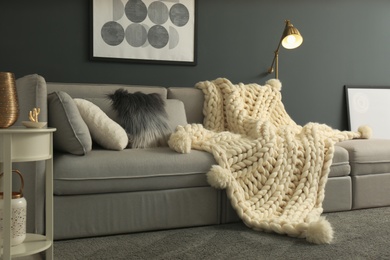 Photo of White knitted plaid on sofa in living room. Interior design