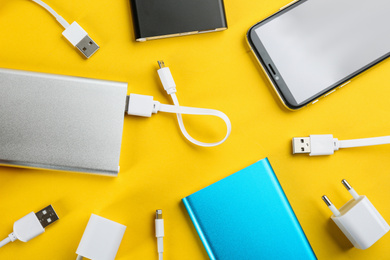 Photo of Mobile phone and portable chargers on yellow background, flat lay