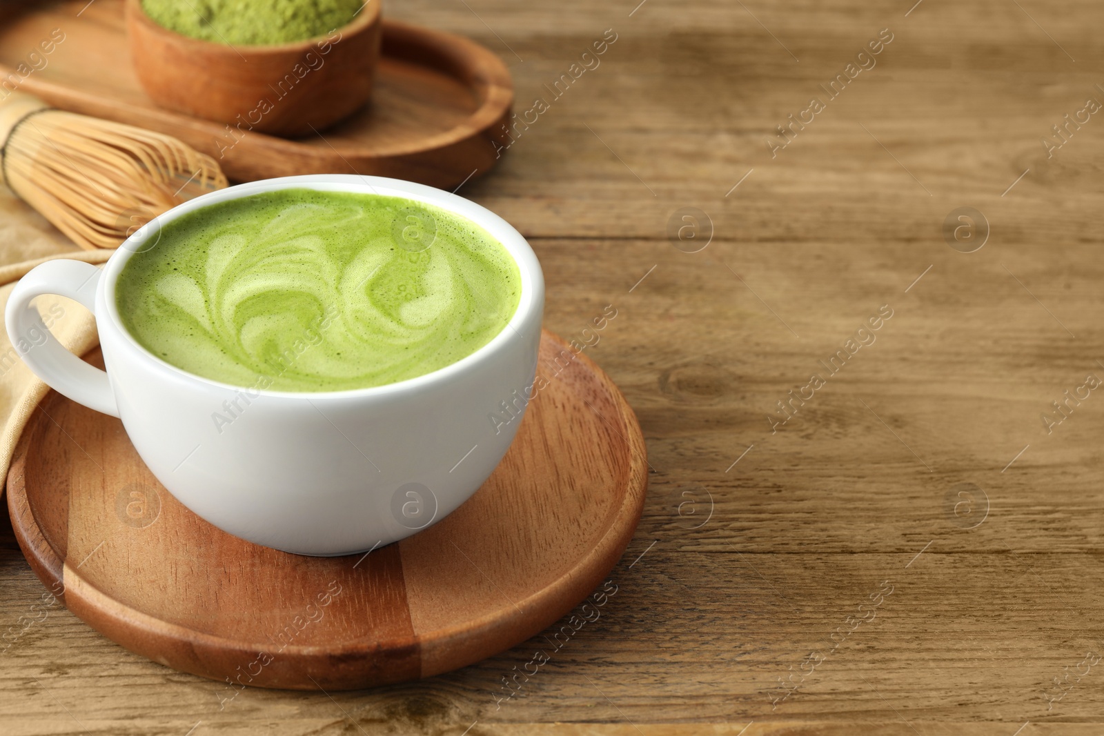 Photo of Cup of aromatic matcha latte on wooden table. Space for text