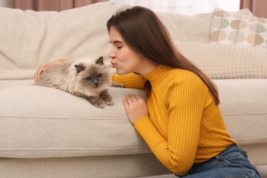 Photo of Woman kissing her cute cat near soft sofa indoors