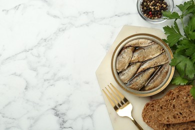 Photo of Tin can with tasty sprats served on white marble table, flat lay. Space for text