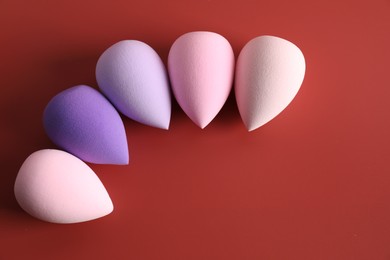 Photo of Many colorful makeup sponges on red background, flat lay. Space for text