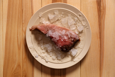 Photo of Piece of fresh raw fish with ice on wooden table, top view