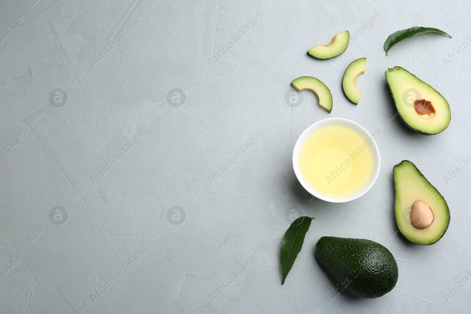 Photo of Bowl of natural oil and avocados on grey stone background, flat lay. Space for text