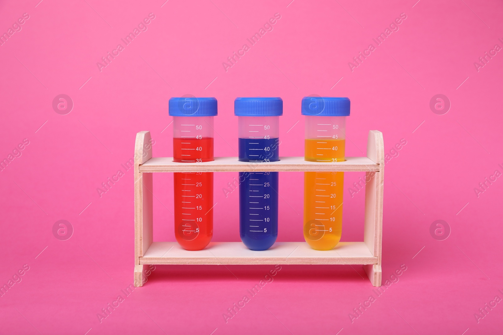 Photo of Test tubes with colorful liquids in wooden stand on bright pink background. Kids chemical experiment set