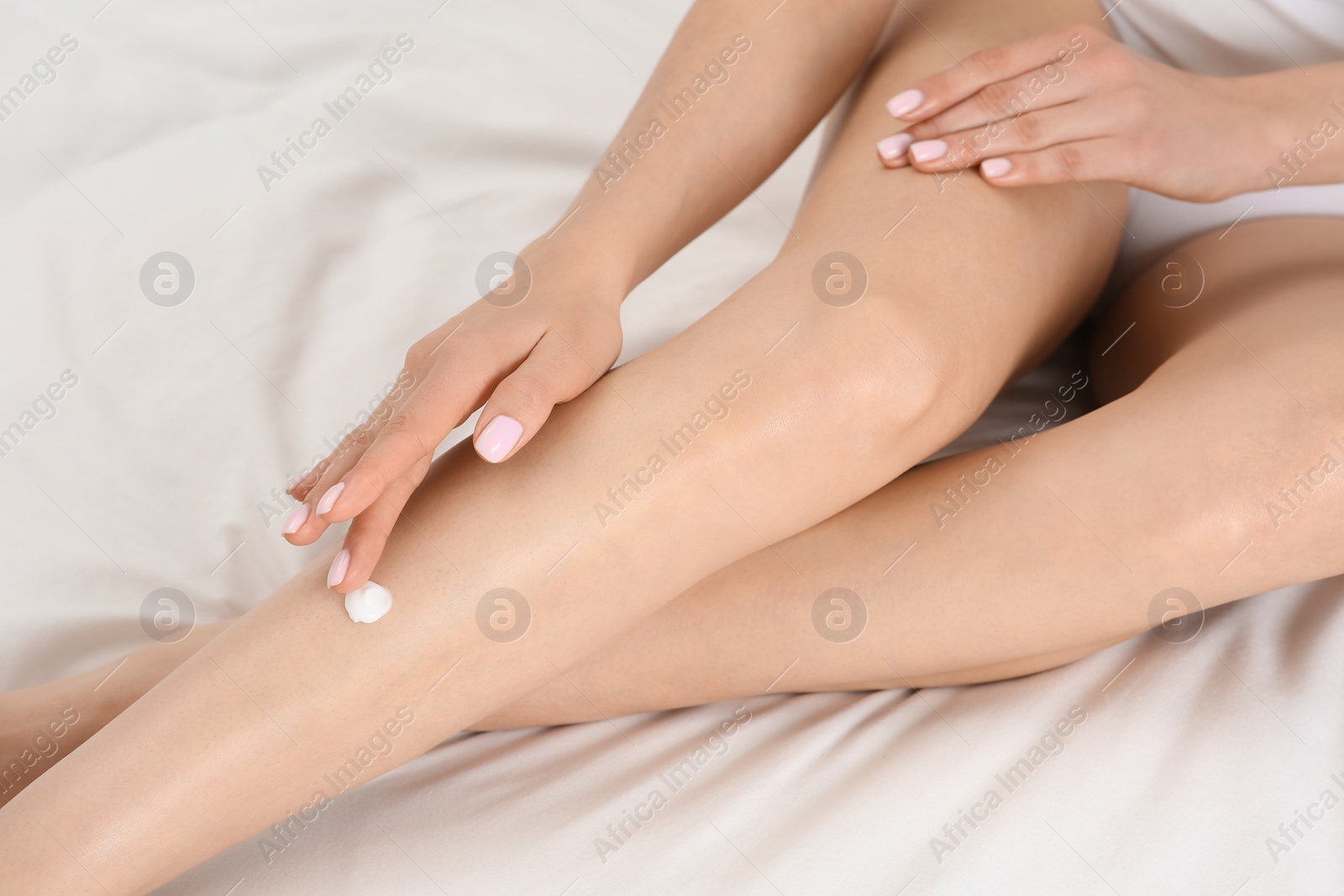 Photo of Woman applying body cream onto her smooth legs on bed, above view