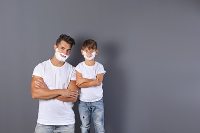 Father and son with shaving foam on faces against color background. Space for text