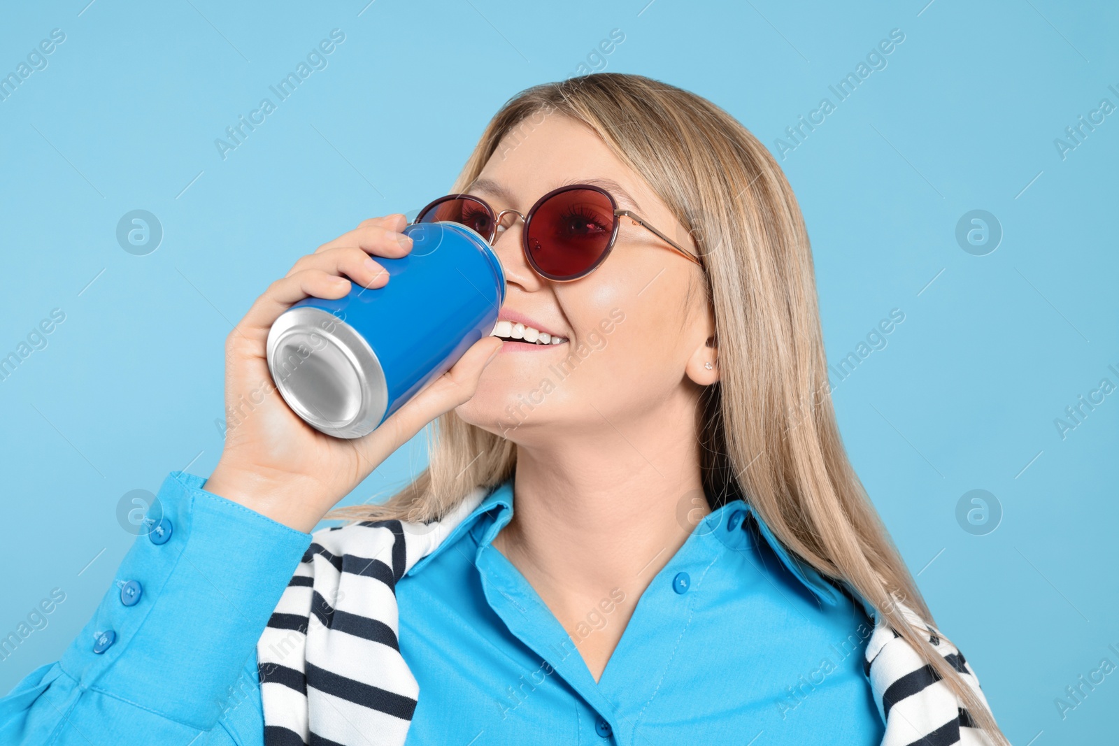 Photo of Beautiful happy woman drinking from beverage can on light blue background