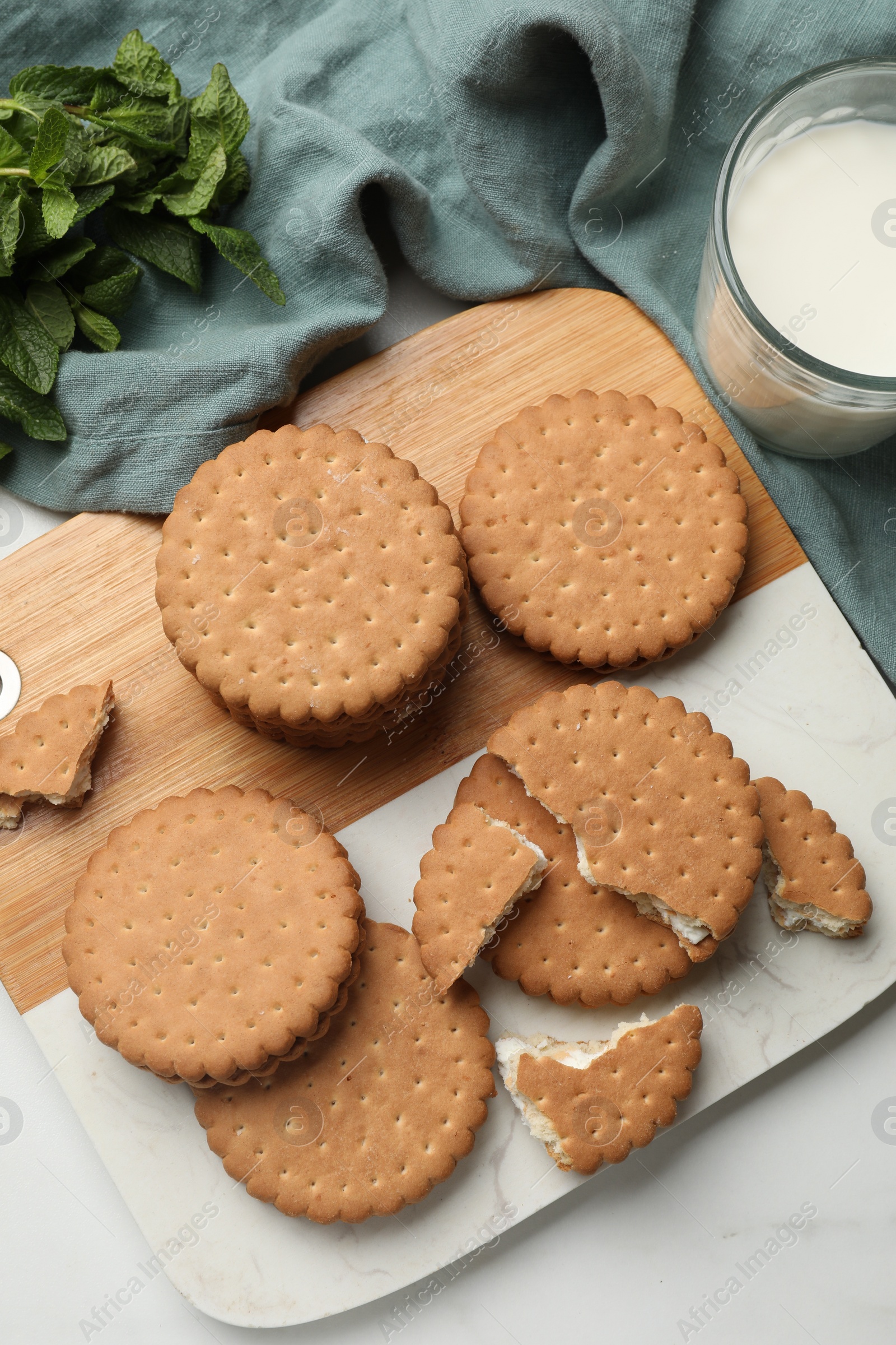 Photo of Tasty sandwich cookies, glass of milk and mint on white table, above view