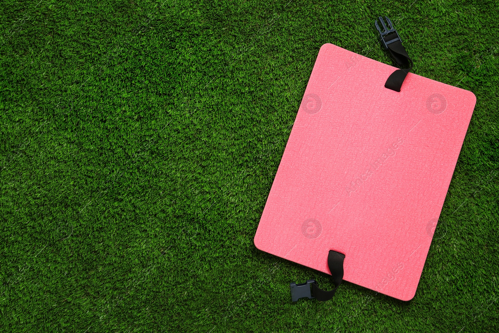 Photo of Pink foam tourist seat mat on green grass, top view. Space for text