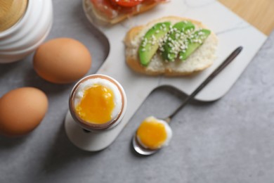 Photo of Fresh soft boiled egg in cup and sandwich with avocado served on grey table, flat lay