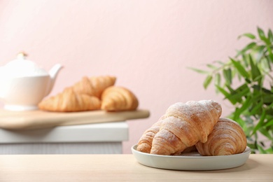 Plate of fresh croissants sprinkled with powdered sugar on table indoors, space for text. French pastry